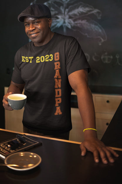 Funny Grandpa Est 2023 Cool T-shirt, black-man-whoisagrandfather-wearing-a-printondemand-family-t-shirt-and-a-beret-having-a-coffee