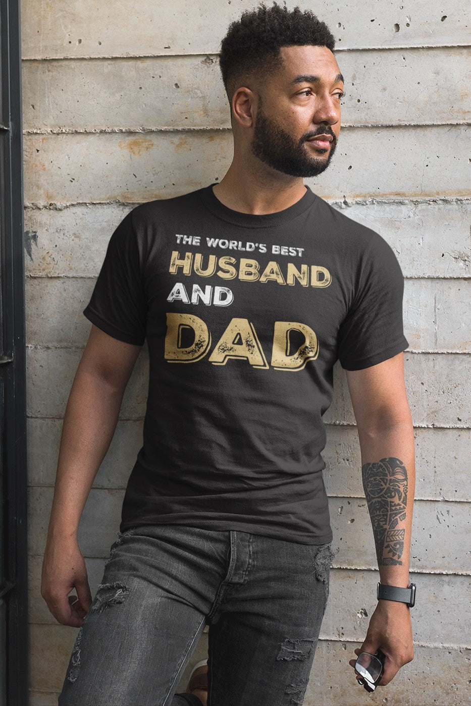 Funny The World’s Best Husband and Dad T-shirt, front-view-t-shirt-mockup-featuring-a-man-with-a-beard-against-a-concrete-wall-and-a-window